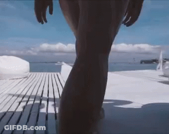 A Woman In A Bikini Is Walking On A Wooden Deck Towards The Ocean GIF