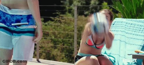 A Woman In A Bikini Sits On A Chair Next To A Man In Swim Shorts GIF