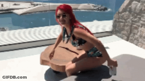 A Woman In A Bikini Sits On A Wooden Table In Front Of A Pool GIF