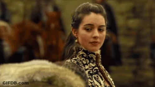 A Woman In A Black And Gold Dress Is Standing In Front Of A Group Of People . GIF
