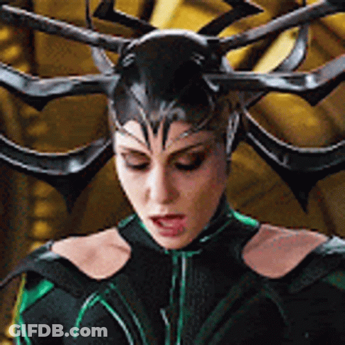A Woman In A Black And Green Costume With Horns On Her Head Is Looking Down . GIF