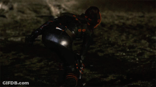 A Woman In A Black And Orange Outfit Is Kneeling Down GIF