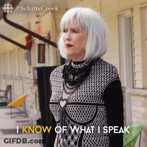 A Woman In A Black And White Dress Says " I Know Of What I Speak " In Front Of A Building GIF