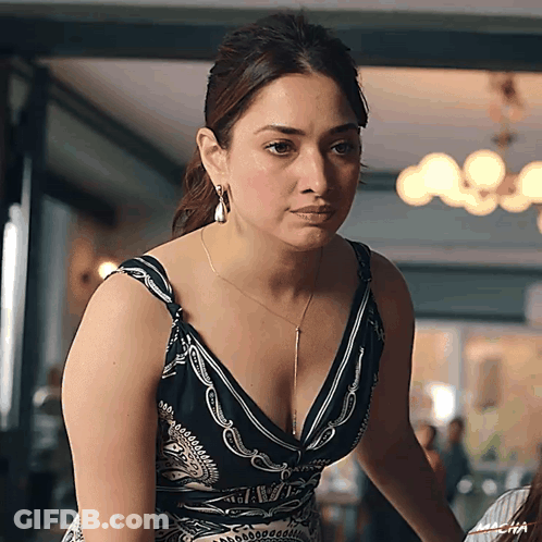 A Woman In A Black And White Dress With A Plunging Neckline Is Looking At The Camera GIF