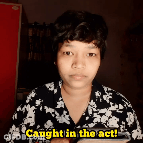 A Woman In A Black And White Floral Shirt Is Holding A Cell Phone And Says Caught In The Act GIF