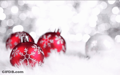 A Woman In A Black And White Floral Shirt Stands In Front Of Christmas Balls GIF