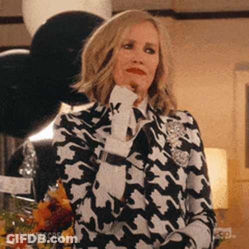 A Woman In A Black And White Houndstooth Suit Holds Her Hand To Her Chin . GIF