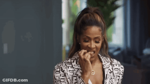 A Woman In A Black And White Jacket Is Eating A Piece Of Food . GIF