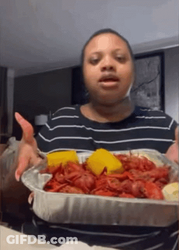 A Woman In A Black And White Striped Shirt Is Holding A Tray Of Crawfish And Cornbread GIF