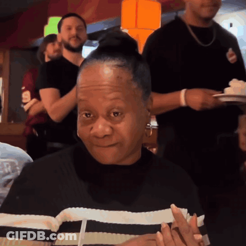 A Woman In A Black And White Striped Shirt Is Smiling In A Restaurant GIF
