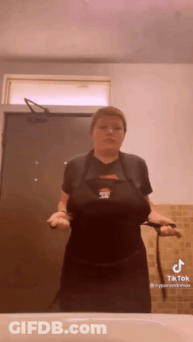 A Woman In A Black Apron Is Standing In Front Of A Sink In A Bathroom . GIF