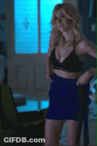 A Woman In A Black Bra And Blue Skirt Is Standing In A Living Room GIF