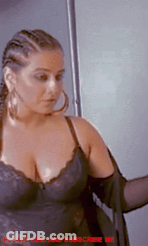 A Woman In A Black Bra And Hoop Earrings Is Standing In Front Of A Door . GIF