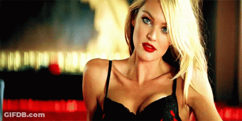 A Woman In A Black Bra And Red Lipstick Is Standing In Front Of A Red Table . GIF