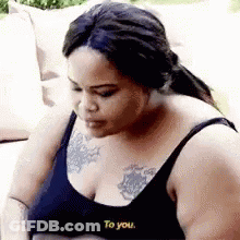 A Woman In A Black Bra Is Sitting On A Couch With A Tattoo On Her Chest . GIF