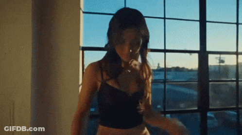 A Woman In A Black Bra Is Standing In Front Of A Window . GIF