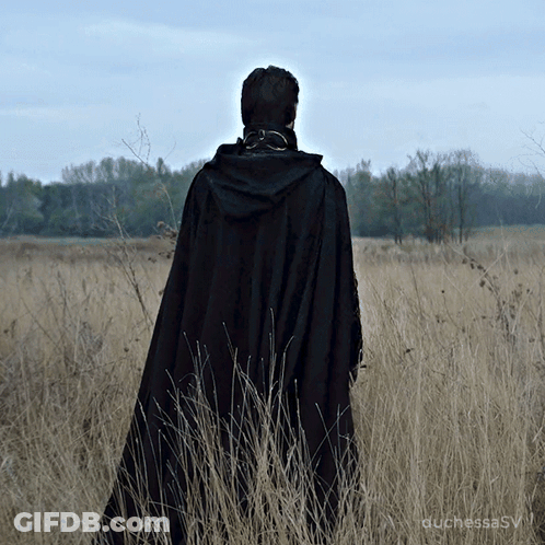 A Woman In A Black Cape Stands In A Field GIF