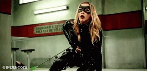A Woman In A Black Catsuit Is Holding An Arrow . GIF
