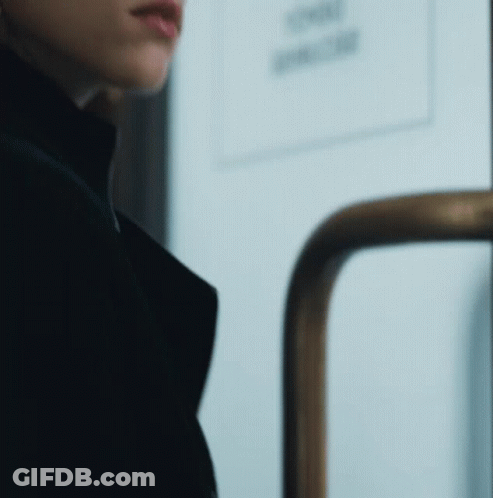 A Woman In A Black Coat Is Standing In Front Of A Door With A Sign That Says Smoking GIF