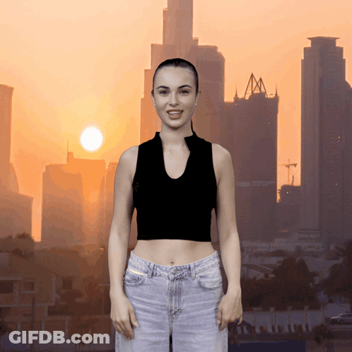 A Woman In A Black Crop Top And Jeans Stands In Front Of A City Skyline GIF