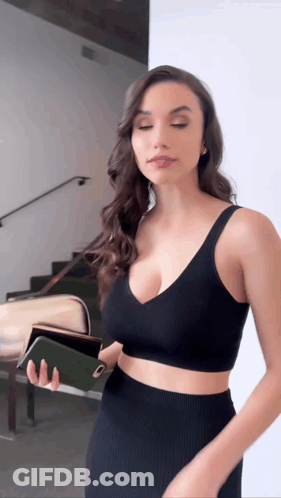 A Woman In A Black Crop Top And Skirt Is Holding A Wallet GIF