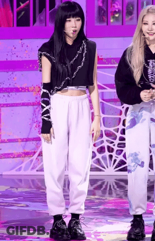 A Woman In A Black Crop Top And White Sweatpants Is Standing On A Stage With Another Woman . GIF