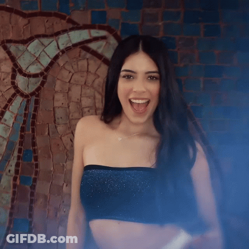 A Woman In A Black Crop Top Is Smiling In Front Of A Mosaic Wall GIF