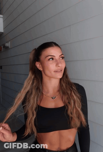 A Woman In A Black Crop Top Is Standing In Front Of A Building GIF