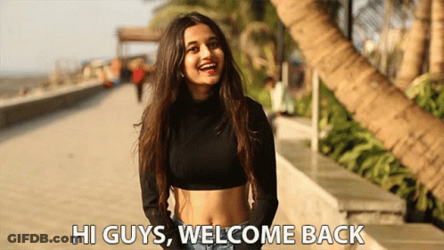 A Woman In A Black Crop Top Is Standing On A Sidewalk And Says Hi Guys Welcome Back GIF