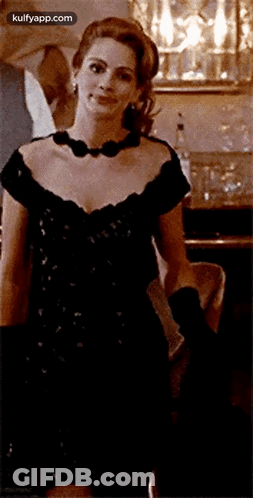 A Woman In A Black Dress And Black Gloves Is Smiling GIF