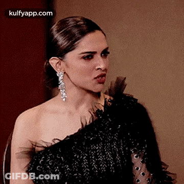 A Woman In A Black Dress And Earrings Is Making A Face . GIF