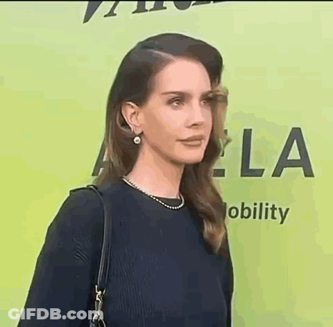 A Woman In A Black Dress And Pearl Earrings Is Standing In Front Of A Green Background . GIF