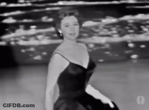 A Woman In A Black Dress And White Gloves Is Dancing On A Stage . GIF