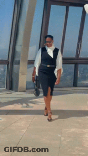 A Woman In A Black Dress And White Shirt Is Standing In Front Of A Window . GIF