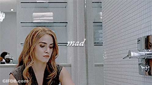 A Woman In A Black Dress Is Adjusting A Shower Head With The Word Mad Written On The Wall Behind Her GIF
