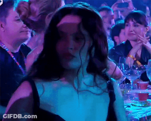 A Woman In A Black Dress Is Dancing In A Crowd Of People GIF