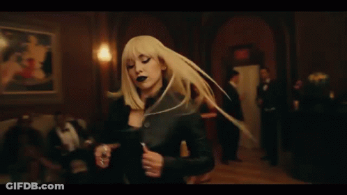 A Woman In A Black Dress Is Dancing In A Room Surrounded By Men In Suits . GIF