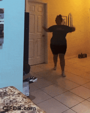 A Woman In A Black Dress Is Dancing In A Room With A Blue Wall GIF