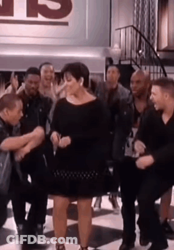 A Woman In A Black Dress Is Dancing In Front Of A Group Of People . GIF
