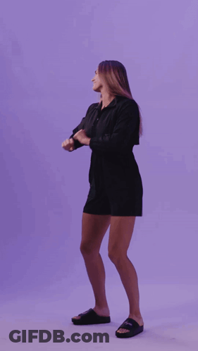 A Woman In A Black Dress Is Dancing In Front Of A Purple Wall GIF