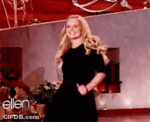 A Woman In A Black Dress Is Dancing On A Stage In Front Of A Wall With The Word Ellen On It . GIF