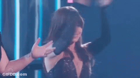 A Woman In A Black Dress Is Dancing On A Stage While A Man Holds Her Hand . GIF
