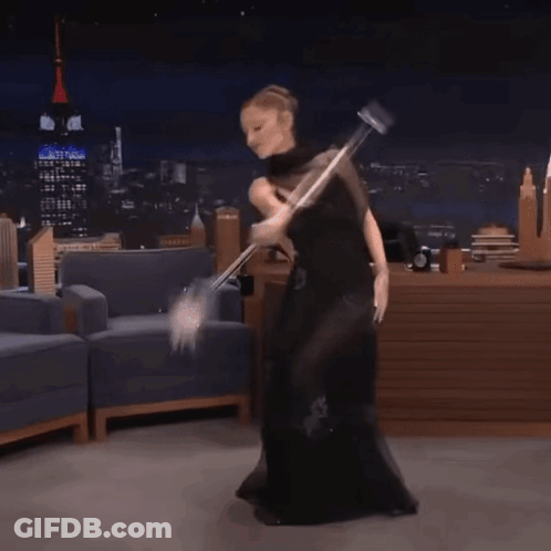 A Woman In A Black Dress Is Dancing With A Mop In Her Hand GIF
