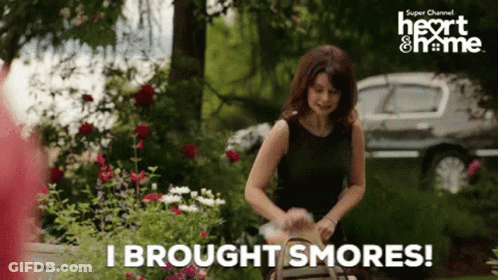 A Woman In A Black Dress Is Holding A Basket And Says " I Brought Smores " GIF