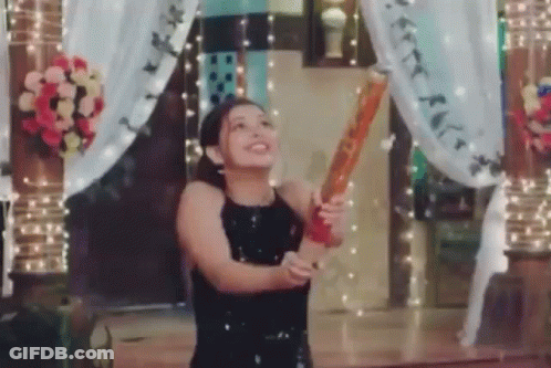 A Woman In A Black Dress Is Holding A Bat In Her Hand And Throwing It In The Air . GIF
