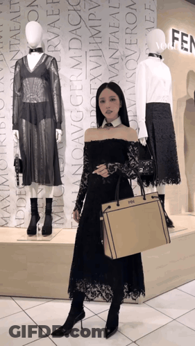 A Woman In A Black Dress Is Holding A Fendi Bag In Front Of Mannequins GIF