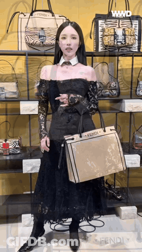 A Woman In A Black Dress Is Holding A Fendi Purse GIF