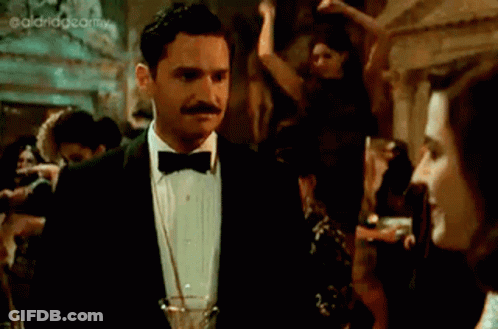A Woman In A Black Dress Is Holding A Glass Of Champagne GIF
