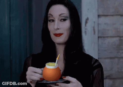 A Woman In A Black Dress Is Holding A Glass Of Orange Juice With A Straw GIF