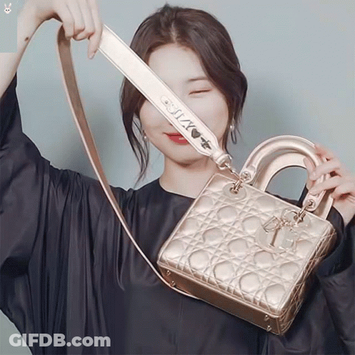 A Woman In A Black Dress Is Holding A Gold Bag With A Strap That Says " I Love You " GIF